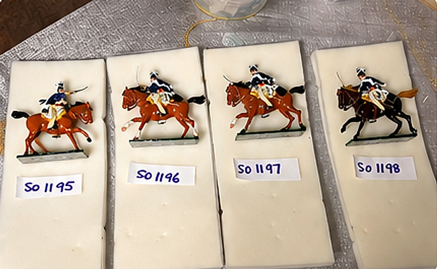 Four painted toy cavalry soldiers laid out on tissue paper with inventory labels